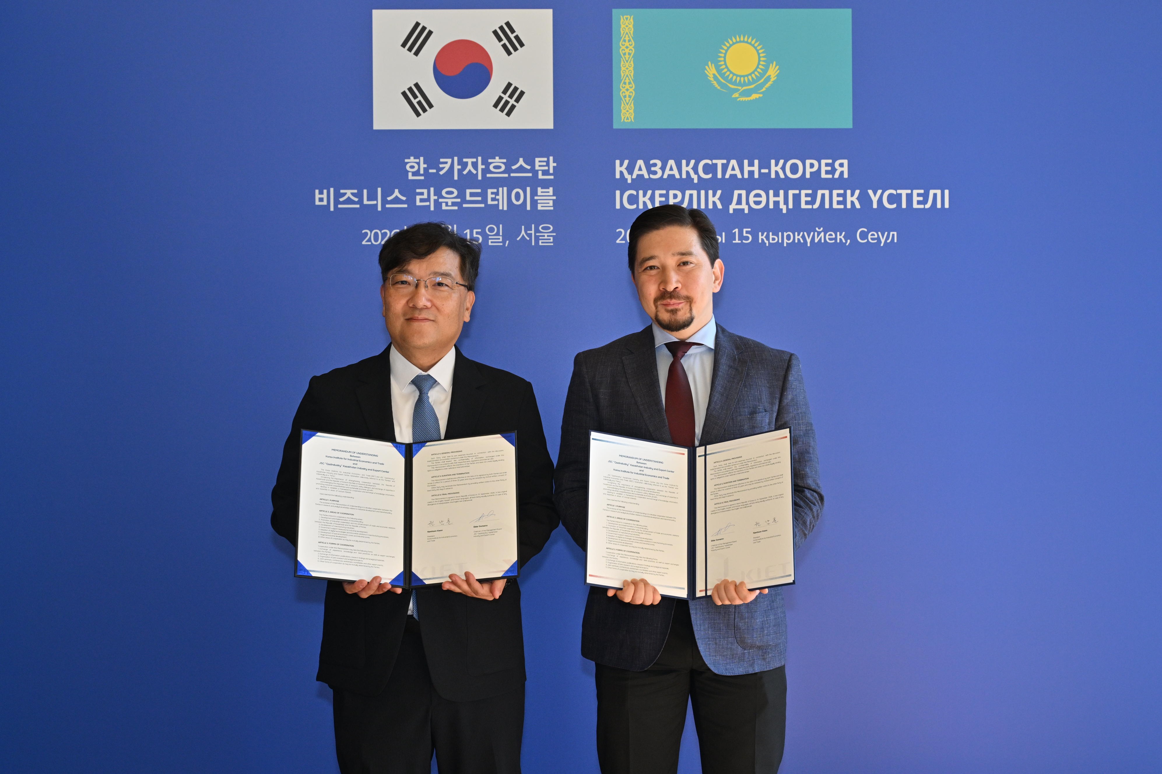 The heads of KIET and QazIndustry holding the signed MOU in front of the Korean and Kazakh flags